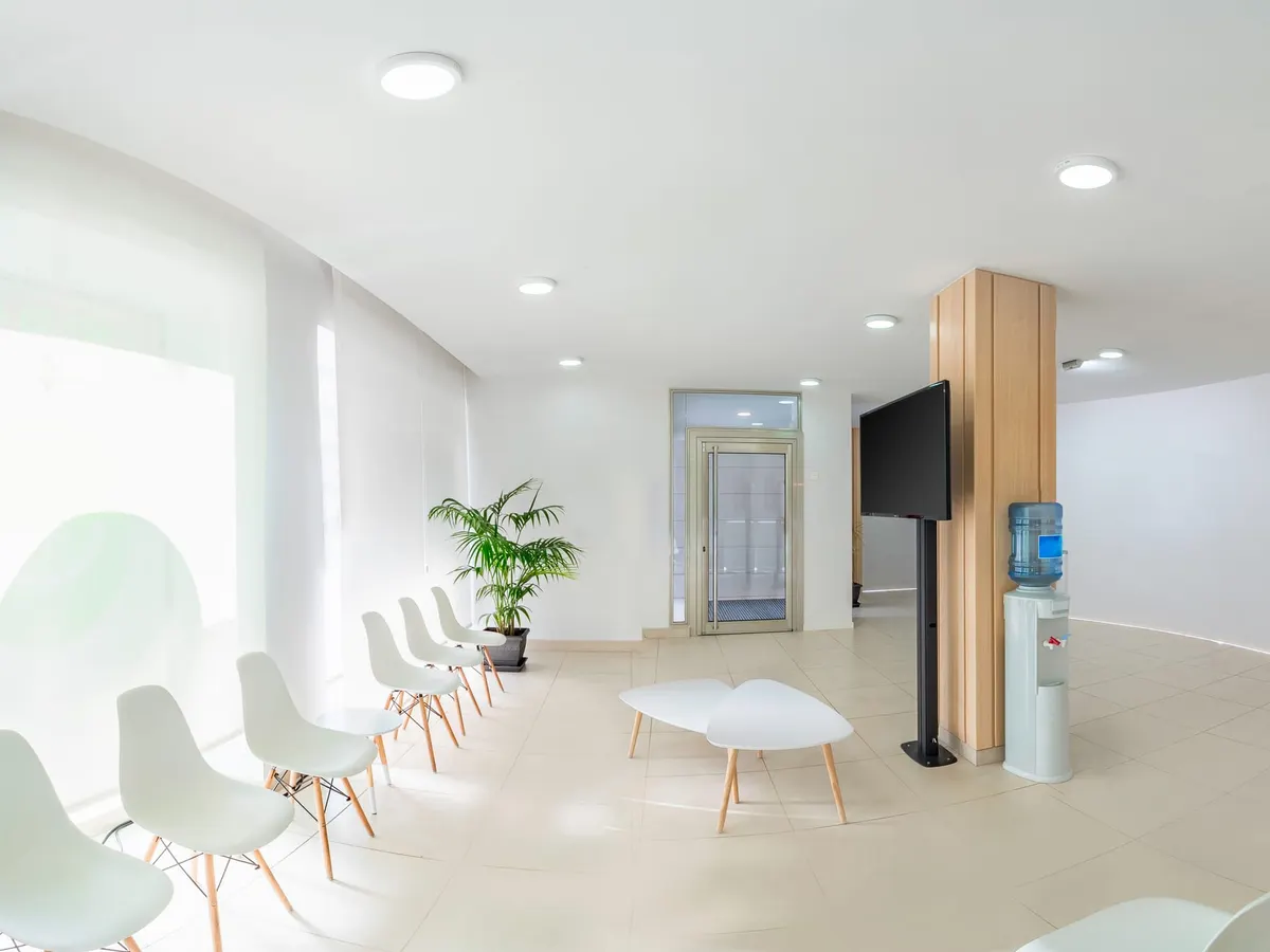Stock photograph: a bright, empty clinic waiting room with white chairs, a potted palm and a curved reception desk