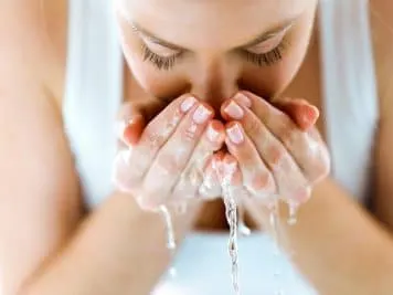 Stock photograph of a model: a woman splashing her face with water cupped in both hands