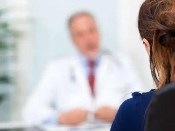 Stock photograph of a model: a woman seen from behind facing a blurred doctor in a white coat and red tie