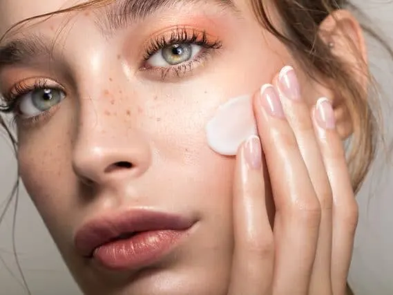 Stock photograph of a model: a woman with freckles touching a dab of cream to her cheek