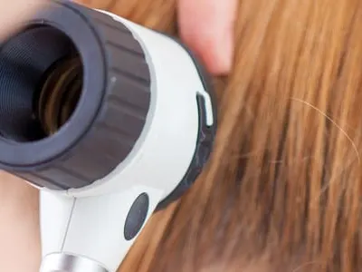 Stock photograph of a model: a clinician holding a dermatoscope up to a woman's ear and hair