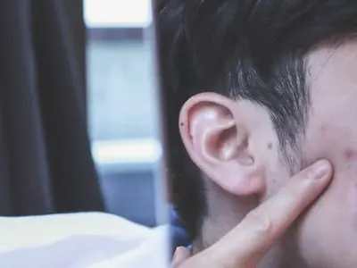 Stock photograph of a model: a young man looking in a mirror, pressing his fingers to his cheek