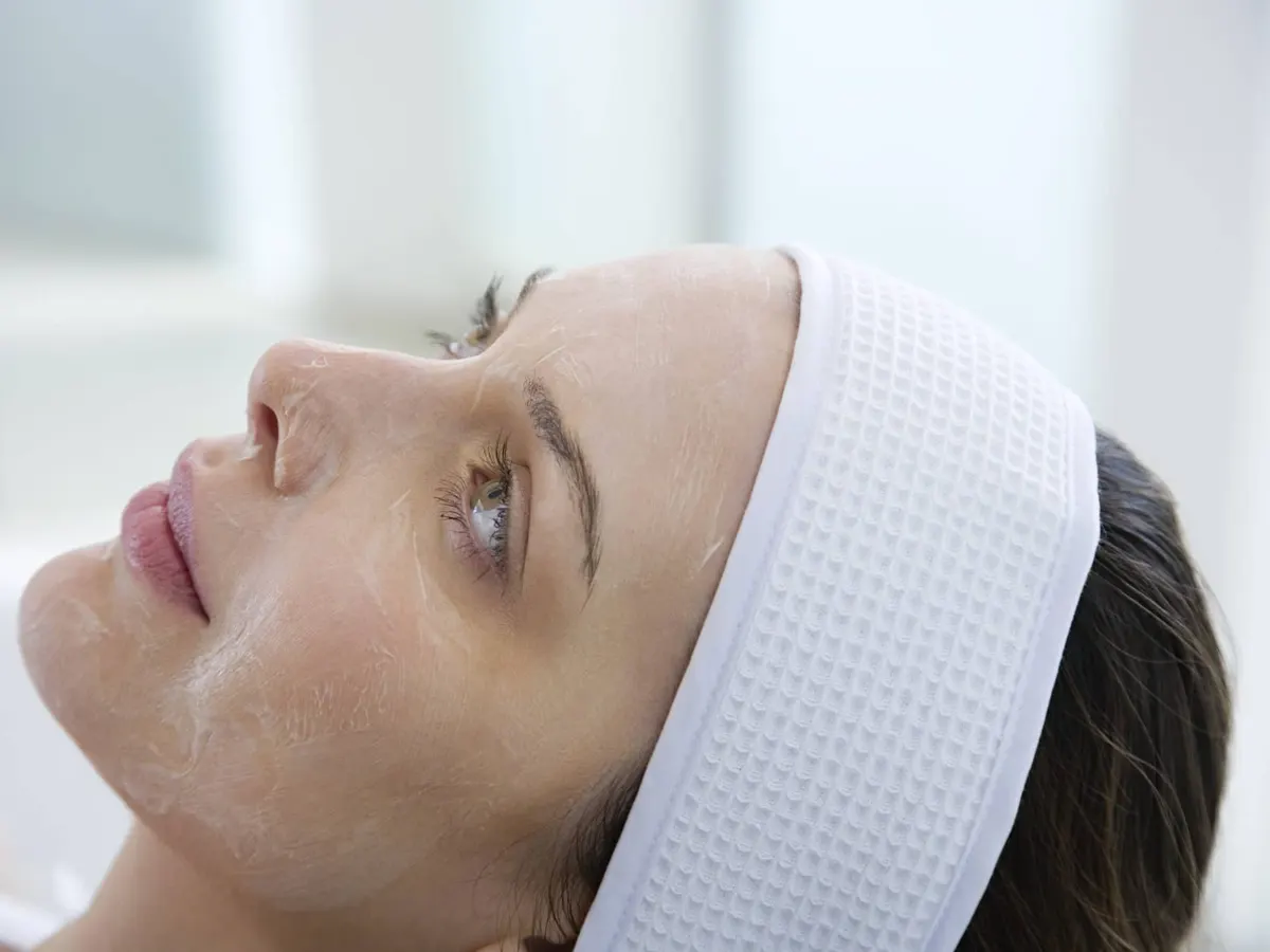 Stock photograph of a model: a woman in a white headband lying back with a thin layer of product peeling on her face