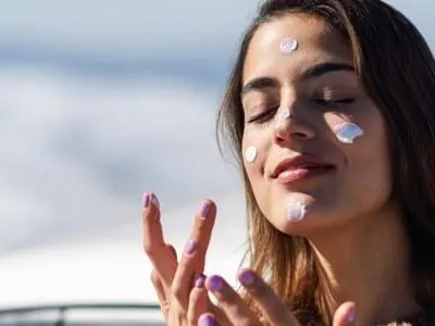 Stock photograph of a model: a woman applying sunscreen to her cheek on a snowy mountain
