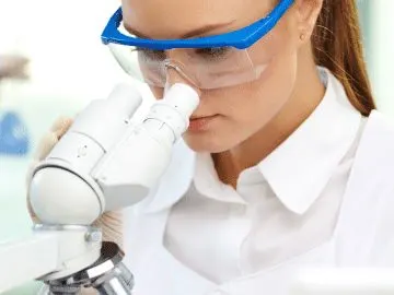 Stock photograph of models: a woman looking through a microscope while a colleague holds a test tube in a lab