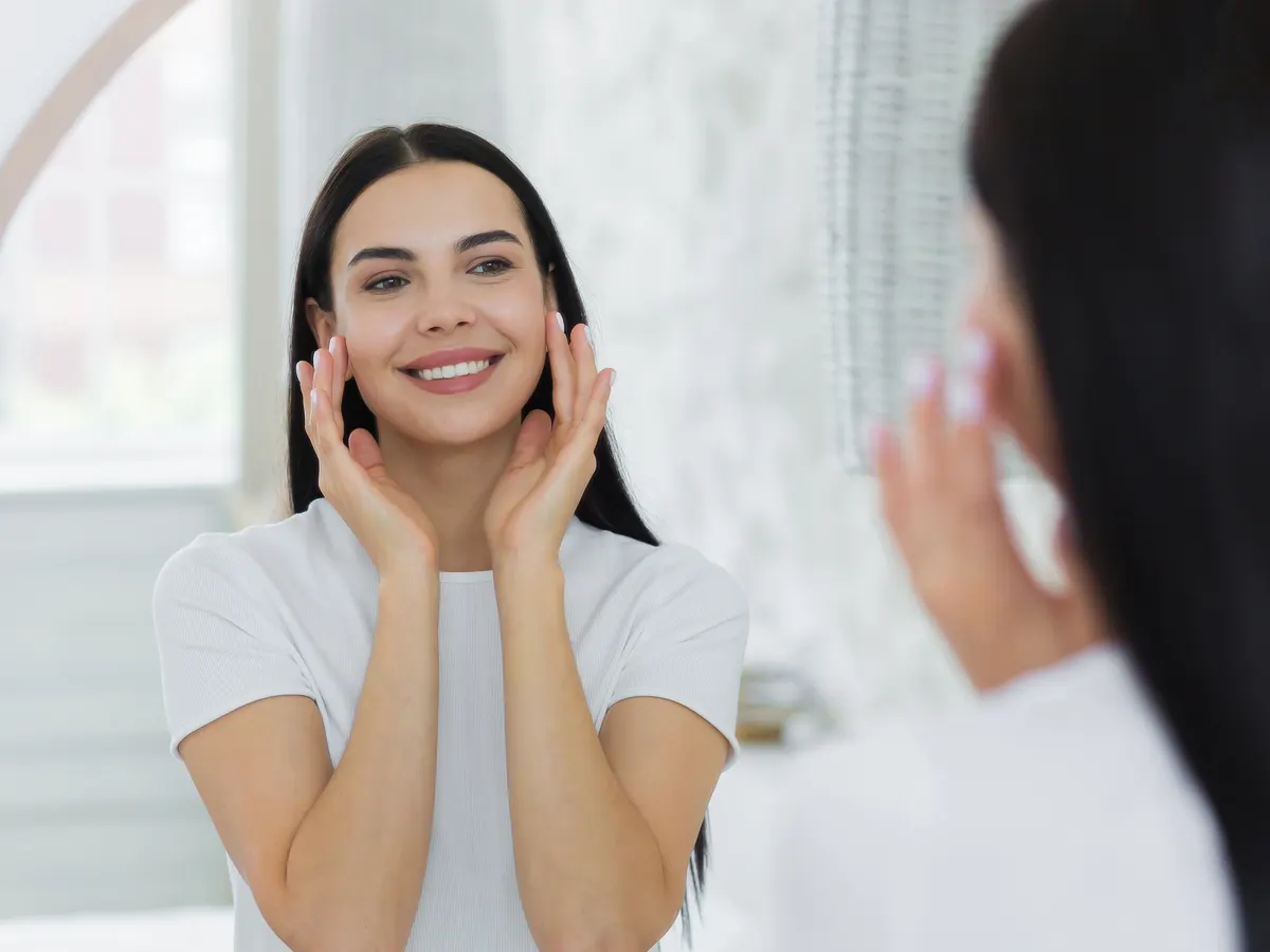 Stock photograph of a model: a smiling woman with long dark hair touching her cheeks in a mirror