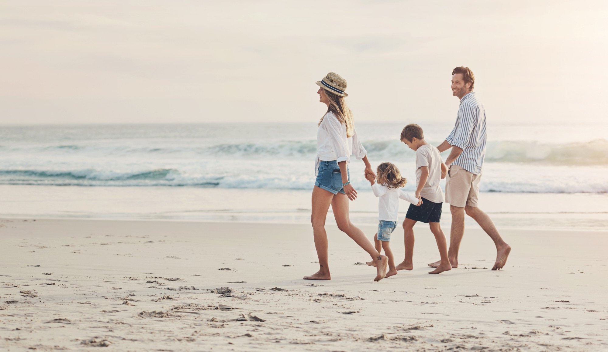 Stock photograph of models: a mother, father and two young children walk hand in hand along a sunny beach