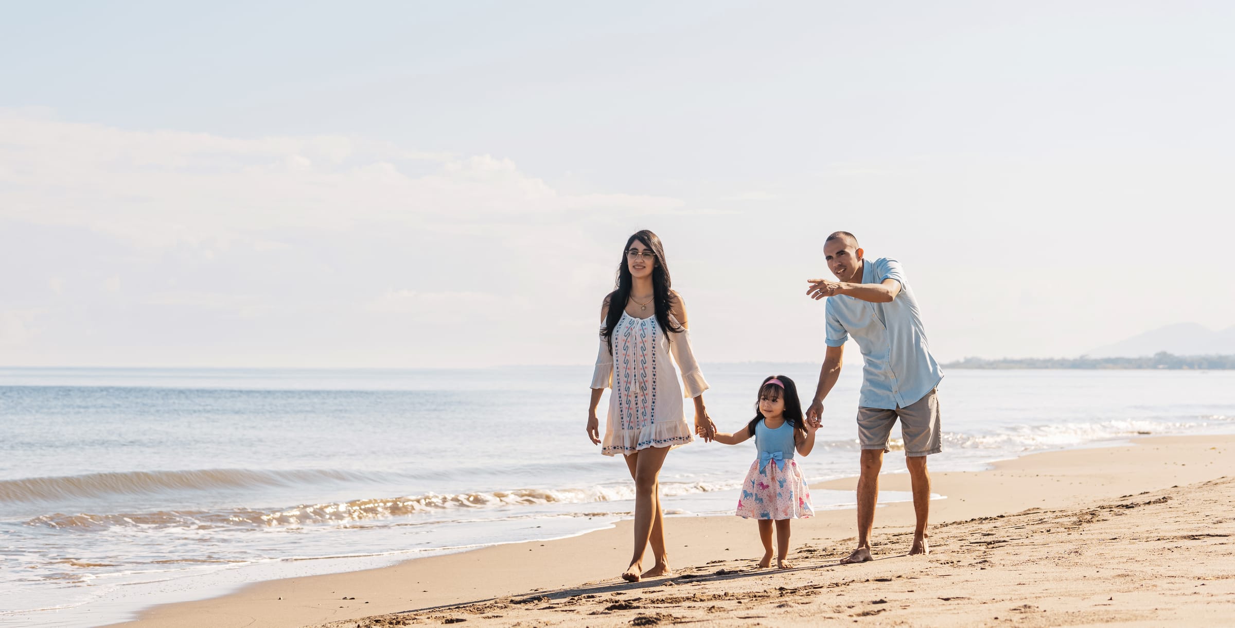 Stock photograph of models: a Latin American mother, father and little girl walk hand in hand along a sunny beach