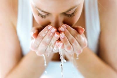 Stock photograph of a model: a woman splashing her face with water cupped in both hands