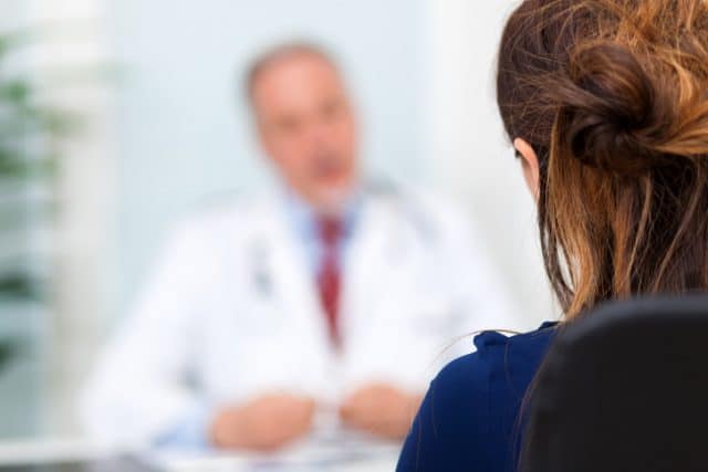 Stock photograph of a model: a woman seen from behind facing a blurred doctor in a white coat and red tie