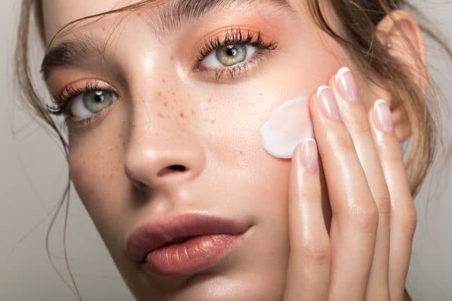 Stock photograph of a model: a woman with freckles touching a dab of cream to her cheek