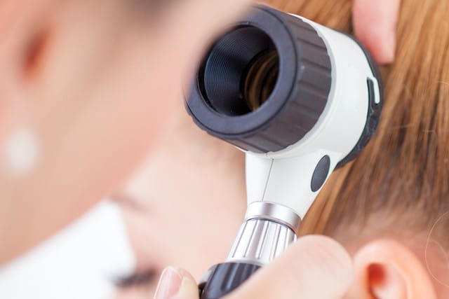 Stock photograph of a model: a clinician holding a dermatoscope up to a woman's ear and hair