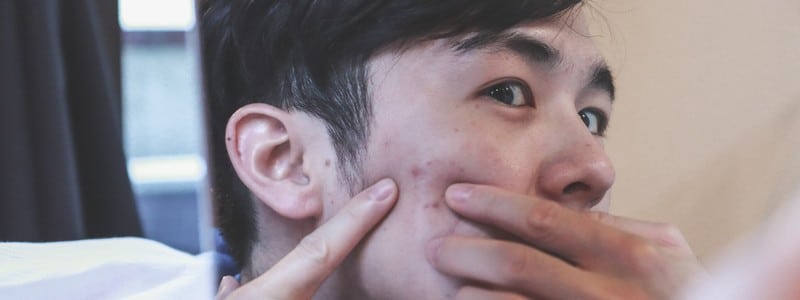 Stock photograph of a model: a young man looking in a mirror, pressing his fingers to his cheek