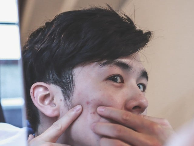 Stock photograph of a model: a young man looking in a mirror, pressing his fingers to his cheek