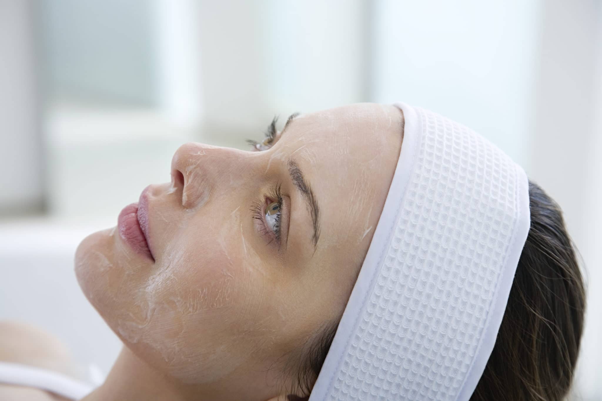 Stock photograph of a model: a woman in a white headband lying back with a thin layer of product peeling on her face