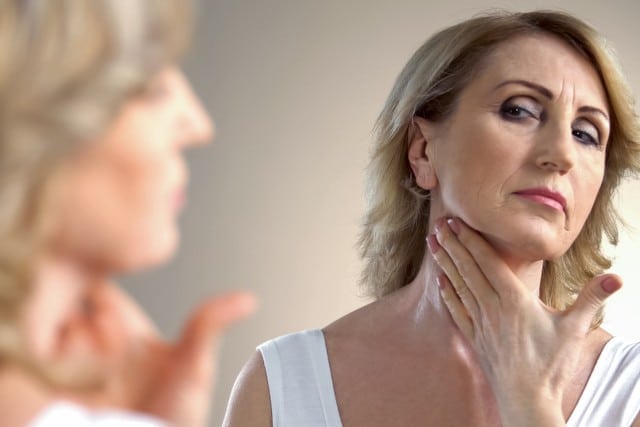 Elderly lady applying anti-age cream on neck, skin care in old age