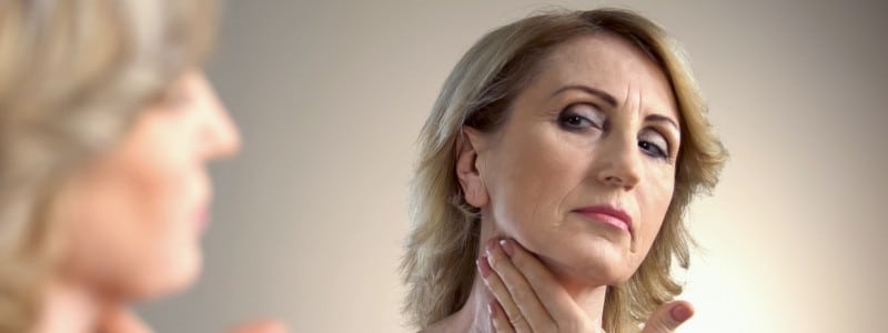 Stock photograph of a model: an older woman looking in a mirror and touching her neck