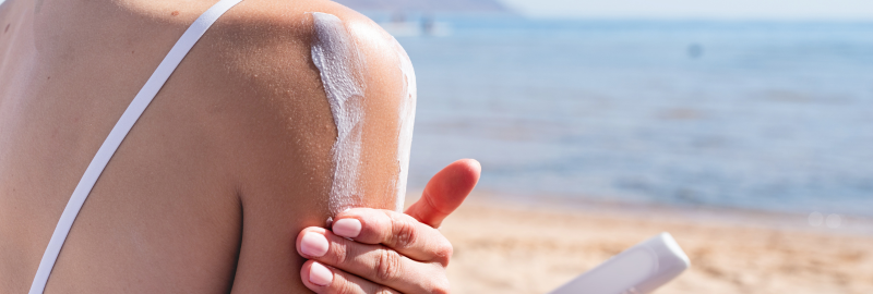 Stock photograph of a model: a woman rubbing sunscreen onto her shoulder on a beach