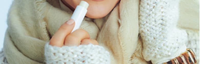 woman in roll neck sweater and cardigan using lip balm in winter.